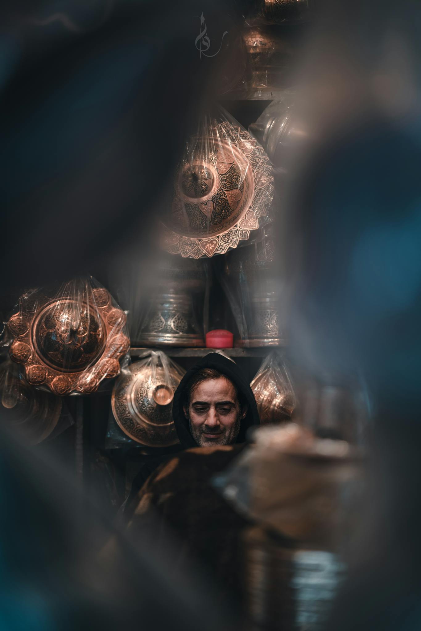 A man surrounded by traditional metal pots in a dimly lit artisan shop.